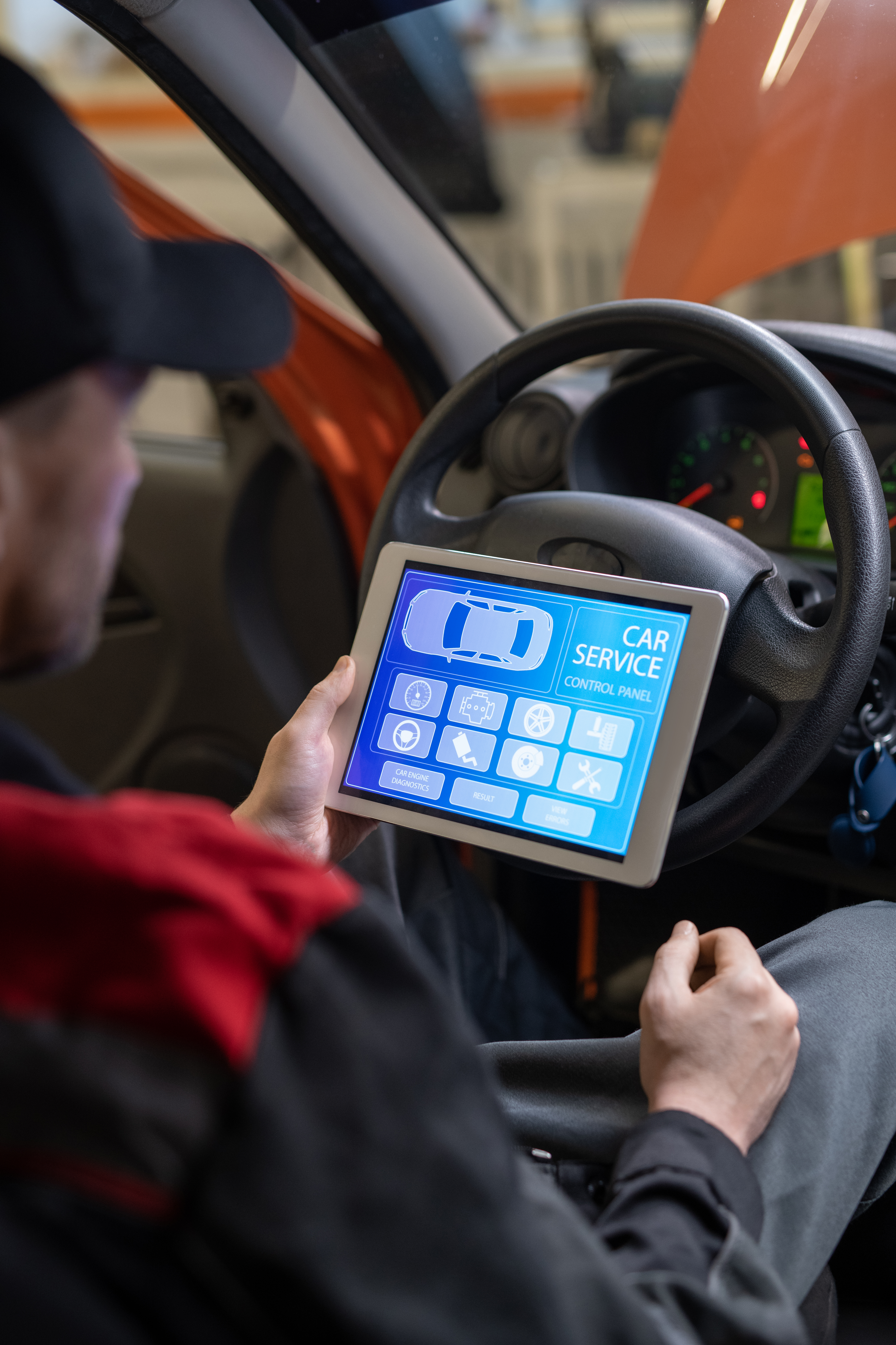 Young repairman with digital tablet sitting in front of steer and looking at icons and options on home page of car service website on screen
